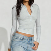 Model wearing a light gray cropped long sleeve polo top styled with denim against a clean studio background.