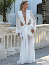 Woman in a white deep V maxi gown with ruched waist and sheer sleeves with a palm tree in the background.