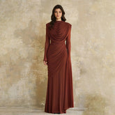 Model wearing a long sleeve maxi gown with a high draped neckline, standing against a textured studio wall with a clean, formal silhouette.