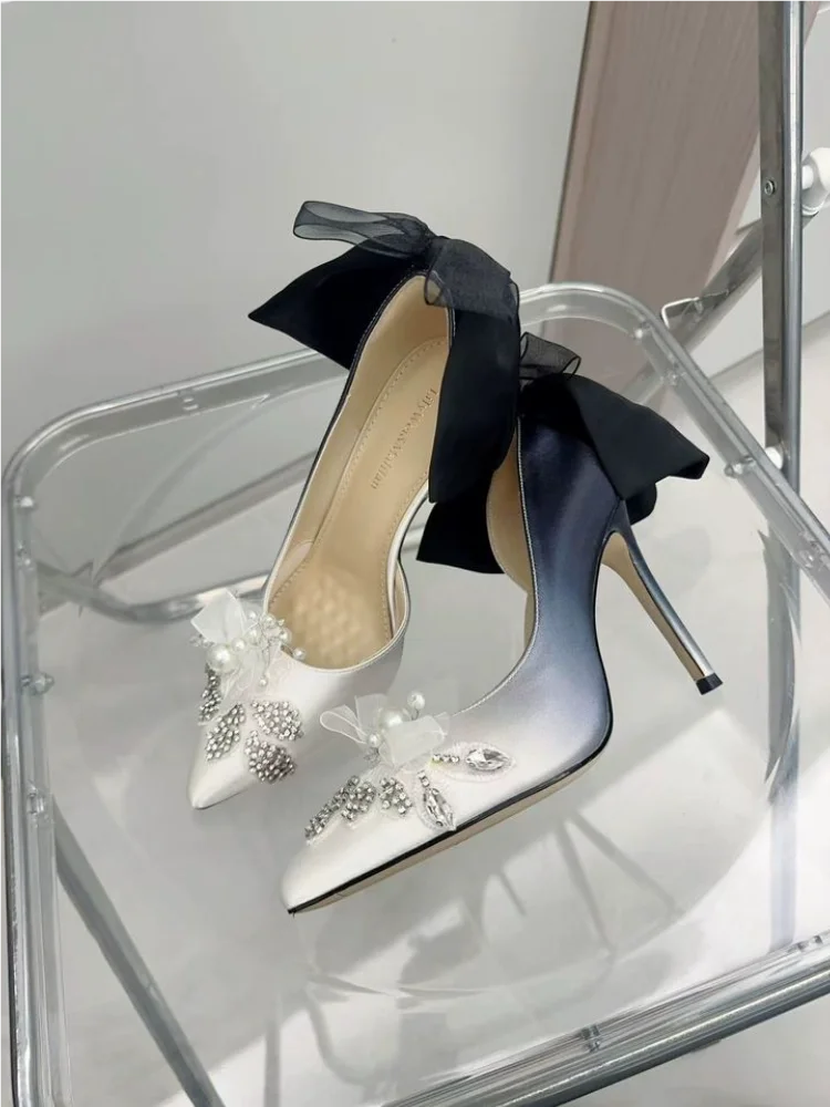 White high-heeled shoes with black bows and embellishments on a clear stand.