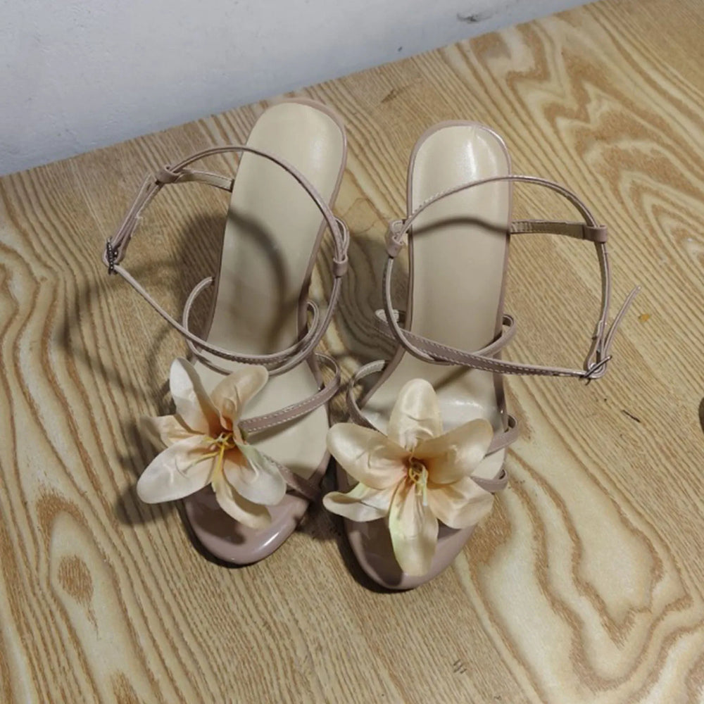 Beige high-heeled sandals with floral decorations on a wooden floor.