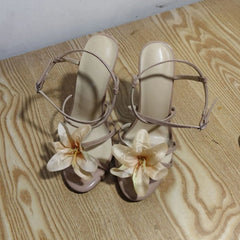 Beige high-heeled sandals with floral decorations on a wooden floor.