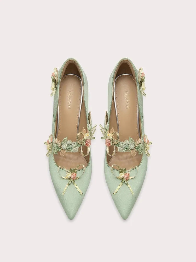 Elegant mint green dress pump with flower applique styled for seasonal celebrations on a light grey background