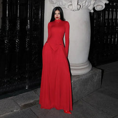 Woman in a elegant red long sleeve maxi dress styled for formal evening parties standing against a dark background