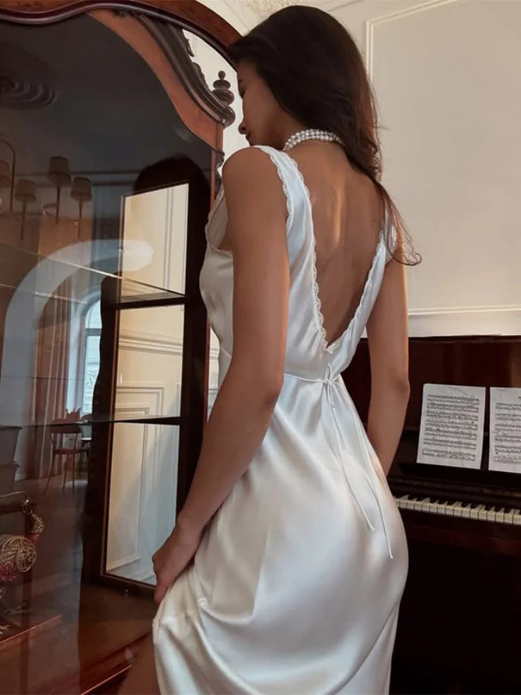 Woman in a elegant white satin dress for evening events and special occasions standing in a room with a mirror and piano.
