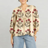 Model wearing a beige embroidered tie-neck blouse styled with denim, standing against a neutral studio background.