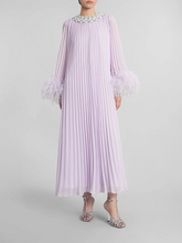 A woman modeling a feather-trimmed pleated midi dress with a round neckline.