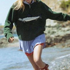 Person wearing a green sweater with a fish design on a beach