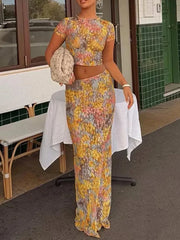 A woman wearing a fitted two-piece floral outfit, perfect for tropical getaways, is standing outdoors near a building entrance.