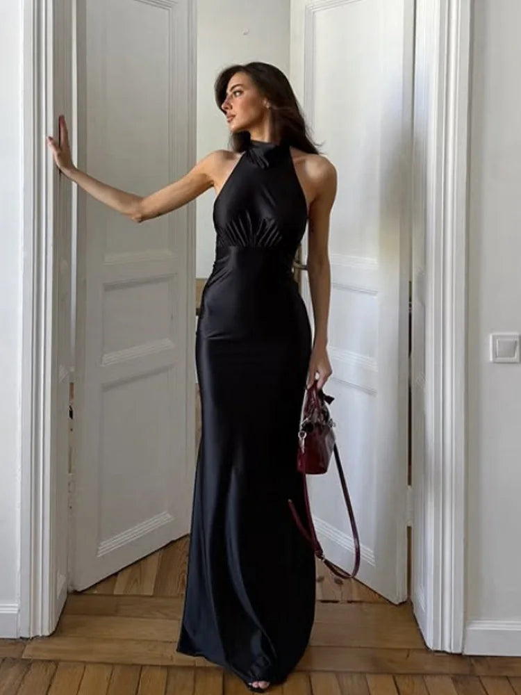 Woman in a black halter satin maxi dress with open back standing in a doorway.