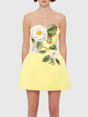 A woman wearing a yellow embroidered floral detailing on a yellow mini dress on a plain background.