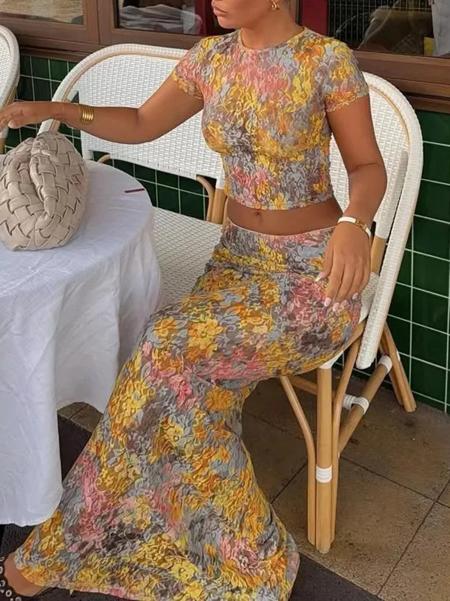 A woman in a Floral mesh crop top and sheer maxi skirt set, styled sitting at an outdoor cafe.