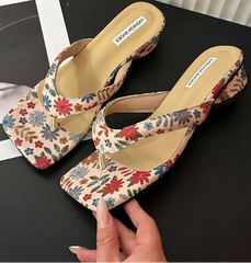 Floral wedge clip toe slides for women, styled for summer beach wear on a black surface with a magazine in the background