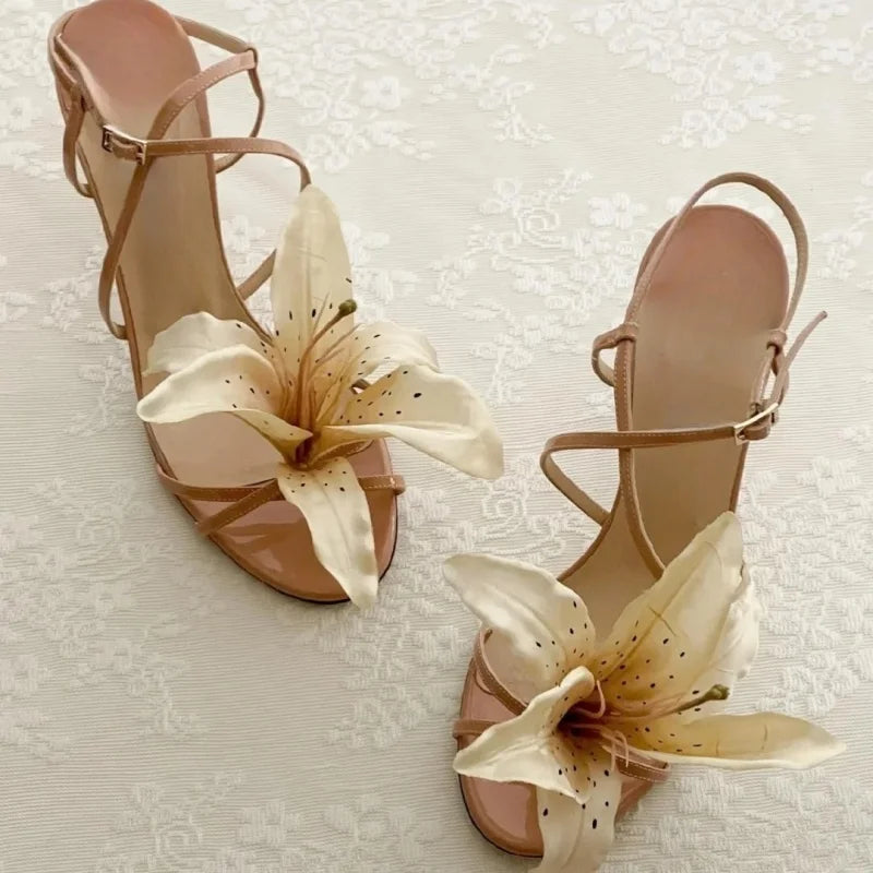 Pair of beige high-heeled sandals with floral decorations on a textured white background