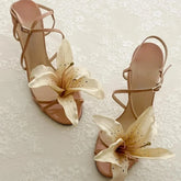 Pair of beige high-heeled sandals with floral decorations on a textured white background