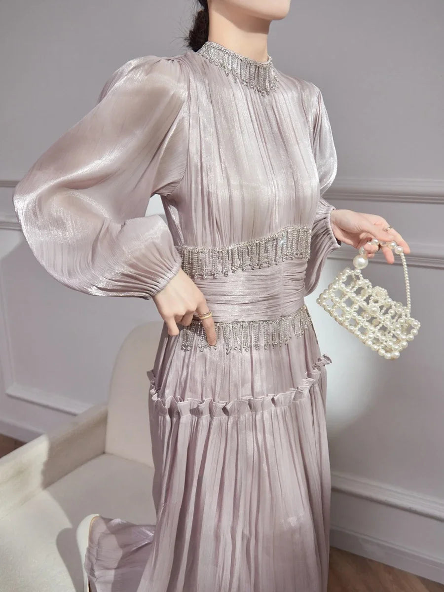 Full look showing the pleated skirt in motion with a structured high neck and long sleeves, styled for an elegant occasion.