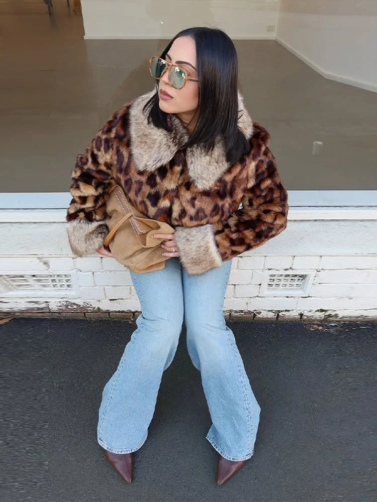Woman wearing a leopard print fur coat and light blue jeans, sitting on a white bench.