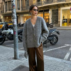 Street-style look featuring a gray fluffy V-neck cardigan worn buttoned up, styled with wide-leg trousers and sunglasses on a city sidewalk.