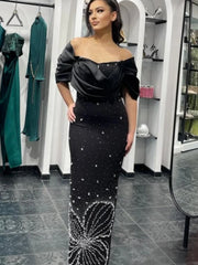 Woman wearing a fold over off the shoulder neckline on a black formal gown for women in a fitting room.