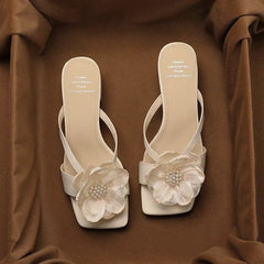 French pearl flip-flops are shown as statement footwear for outdoor parties. Pair of white high-heeled sandals with floral decorations on a brown fabric background