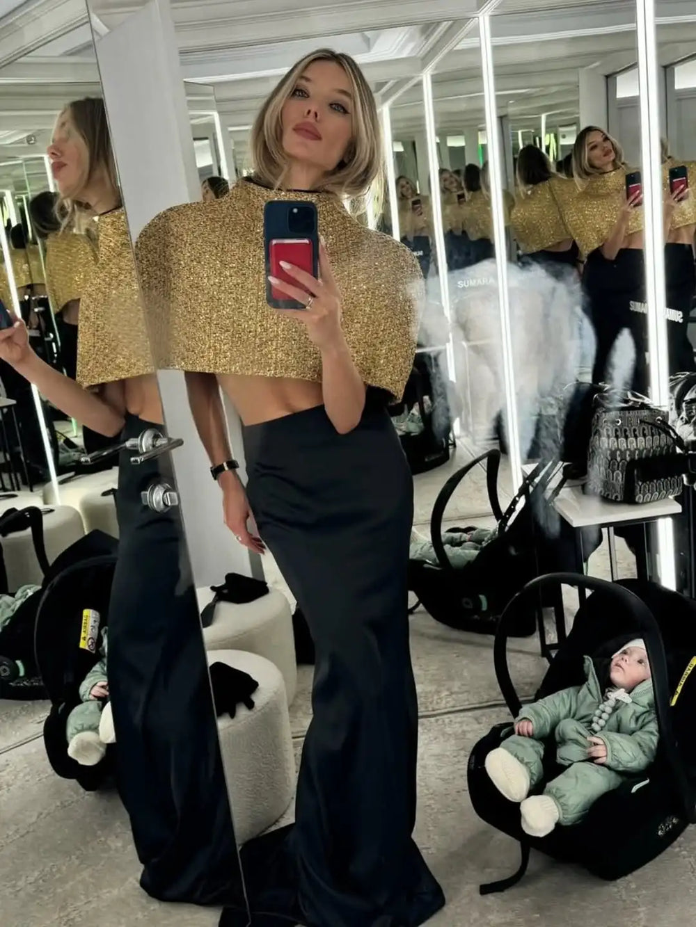 Detail view of the light-catching gold texture on a cape-sleeve top, showing the structured drape and refined finish.