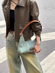 Person holding a light gold emblem detail on a retro denim underarm handbag on a street.