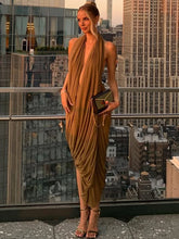 Model wearing a gold ruched halter dress with an open back on a rooftop