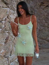 Woman wearing a green knitted mini dress with pearl starfish appliqués with starfish patterns against a stone wall.
