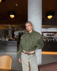 Woman in a green suede zip bomber jacket styled for autumn and winter streetwear, standing in a modern interior setting