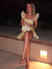 Woman in a  yellow A-line ruffle skirt with matching crop top for women sitting on a ledge at night.