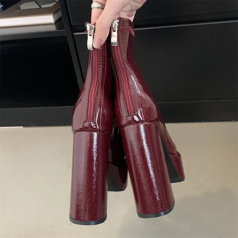 Burgundy patent leather shoes with zippers held by a hand on a neutral background