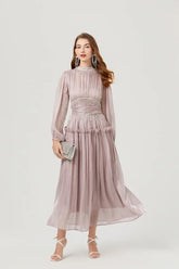 Model wearing a light silver chiffon midi dress with a high neckline and long lantern sleeves, holding the skirt to show movement.