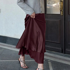 A person wearing a high-waist skirt with a mesh hem in an elegant wine tone is standing in front of a door.