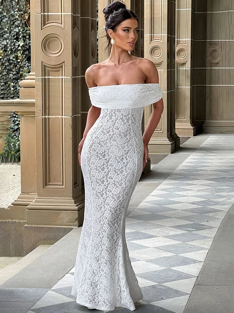 Woman in a white lace off-shoulder gown standing in an elegant outdoor setting.