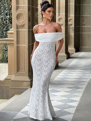 Woman in a white lace off-shoulder gown standing in an elegant outdoor setting.