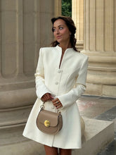 Front view showing the high neckline, long sleeves, and statement buttons on an ivory A-line mini dress in natural daylight.