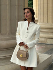 Front view showing the high neckline, long sleeves, and statement buttons on an ivory A-line mini dress in natural daylight.