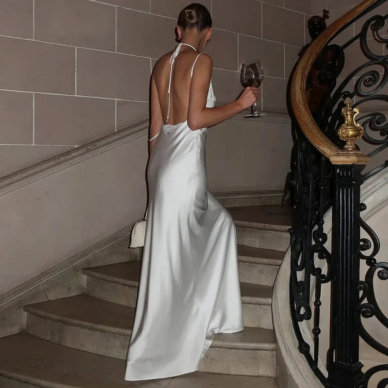 Woman in a junior romantic white lace maxi dress displayed with scenic background descending a staircase holding a glass of wine.