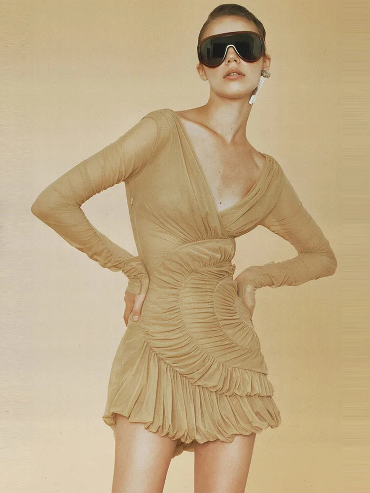 Woman wearing a khaki mesh-pleated bodycon mini dress with long sleeves and sunglasses on a beige background