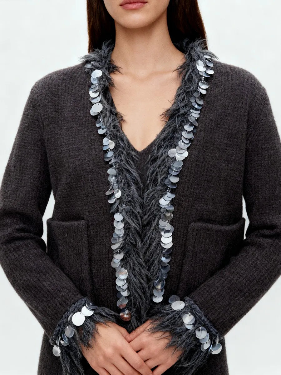 Close-up of neckline showing textured tassel fringe and sequin trim on a soft knit jacket.