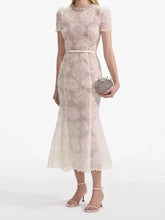 A woman modeling a lace mini dress with a belted waist and a round neckline.