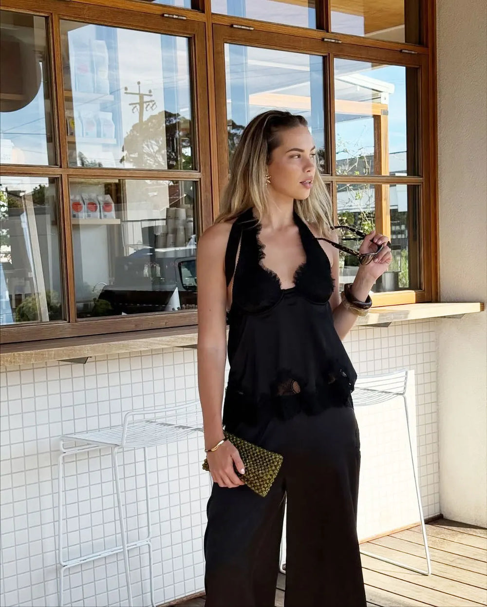 Woman in a black outfit standing in a modern indoor setting with large windows.