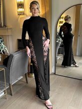 Woman in a black dress with lace detailing standing in a room with a mirror reflection.