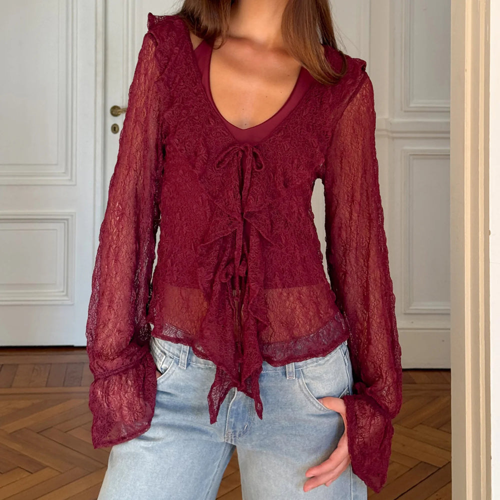 Model wearing a burgundy sheer lace tie-front blouse styled with denim in an indoor setting.
