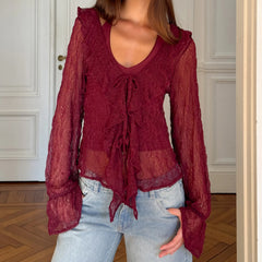 Model wearing a burgundy sheer lace tie-front blouse styled with denim in an indoor setting.