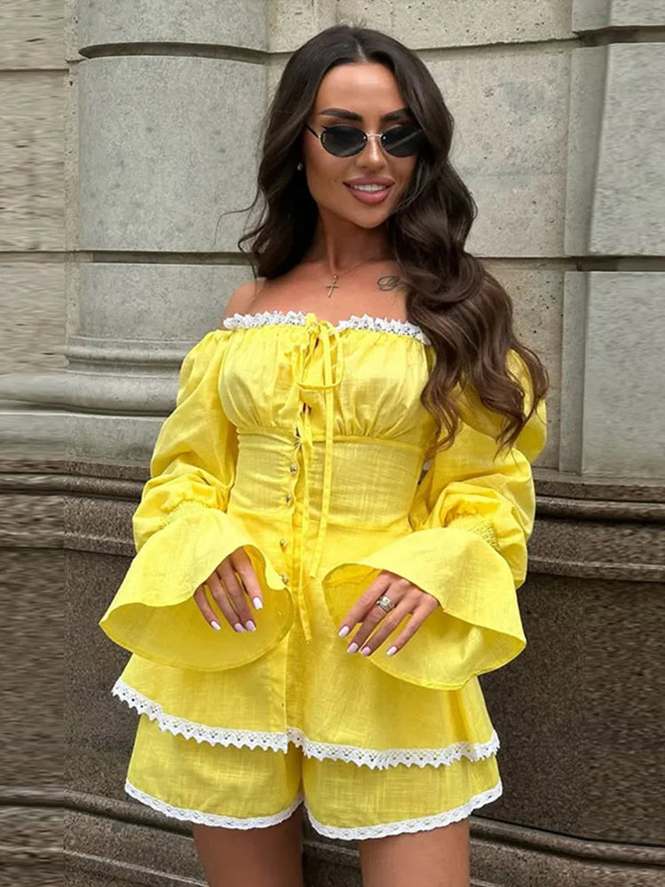 Woman wearing a lace-trimmed trumpet sleeve top and matching shorts standing against a stone wall.