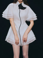 White mini dress with lapel collar and bow at neck on a black background