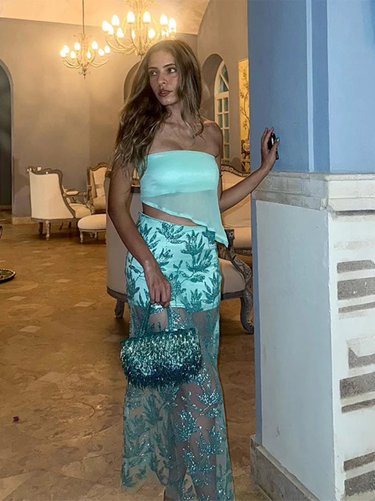 Woman in a mesh leaf-pattern party outfit in a two-piece co-ord standing in an elegant room with a chandelier.