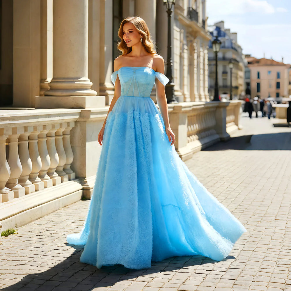 Model wearing a light blue off-shoulder tulle A-line gown with a side slit on a city street
