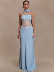 Model wearing a light blue strapless maxi dress with a scarf-style neck detail and sheer lace waist panel against a warm beige backdrop.